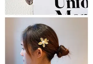 Detail of a gold flower hair clip with pearl center worn by a model on the side