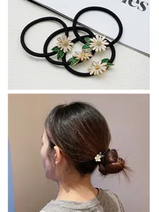 Detail of white daisy hair ties with enamel petals and green leaves on black elastic bands