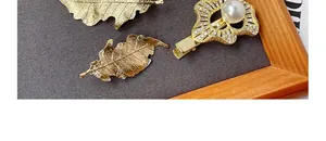 Detail of golden hair clips with realistic leaf designs and pearls on a velvet tray