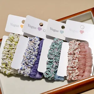 Set of six floral and solid chiffon scrunchies displayed on elegant cards in a wooden tray