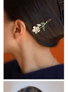 Detail of floral hair clip with white petals and green enamel leaves on dark hair
