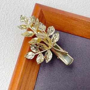 Minimalist golden leaf branch hair clip with detailed leaf texture on dark wood background