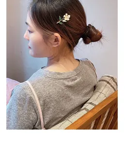 Detailed view of a white flower hair clip with green leaves worn on a woman's hair