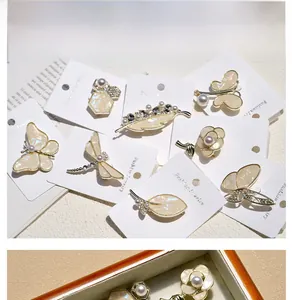 Detailed close-up of shell butterfly brooches and pearl pins on a wooden display tray