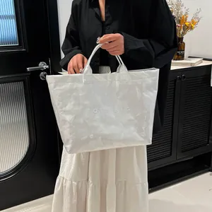 Metallic silver tote bag with embossed letters and glossy finish held by a model