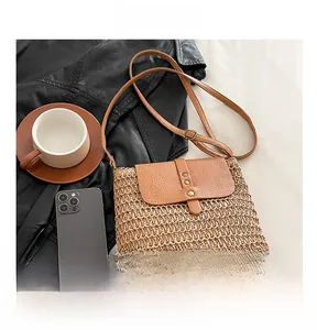 Close-up of straw woven crossbody bag with leather flap and rivet accents on a flat lay