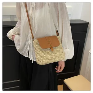 Detail view of handmade straw crossbody bag with brown leather flap and golden rivets