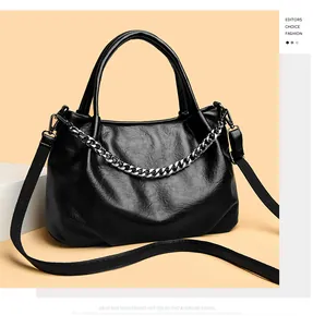 Close-up of black leather tote bag featuring a decorative silver chain and dual handles
