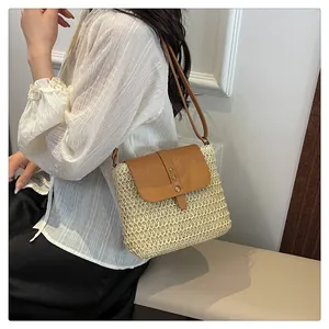 Close-up of hand-woven straw crossbody bag with brown leather flap and metal buckle