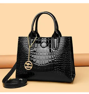 Detail of glossy black patent leather handbag with crocodile pattern and golden charm