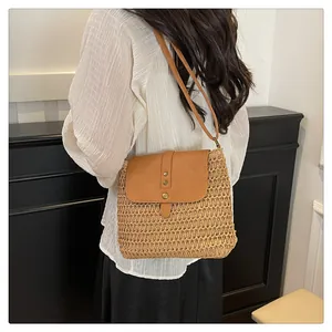 Detail of woven straw shoulder bag featuring a brown leather flap and metal rivets