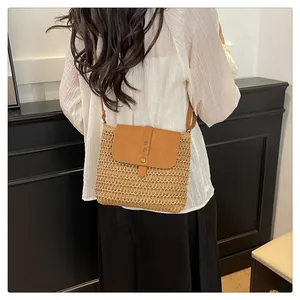 Detail of straw woven crossbody bag with brown leather flap and bronze rivets