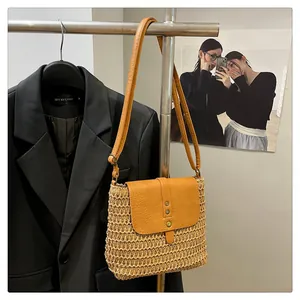 Detail of hand-woven straw crossbody bag with leather flap and metallic rivets