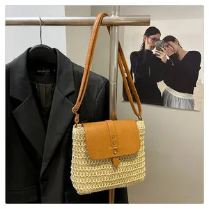 Detail of woven straw crossbody bag with brown leather flap and adjustable strap