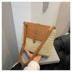 Close-up of woven straw crossbody bag with brown leather flap and golden rivet details
