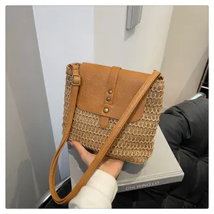 Close-up of handmade straw crossbody bag with brown leather flap and retro metal buckles