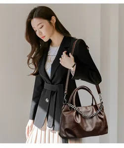 Detail of dark brown tote bag featuring silver chain and soft leather texture on a model