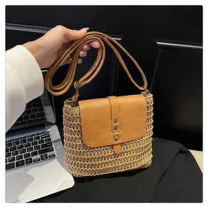 Close-up of handmade beige woven straw crossbody bag with brown faux leather flap and rivets