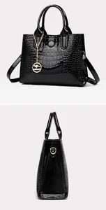 Detail view of glossy black patent leather handbag with crocodile pattern and golden logo