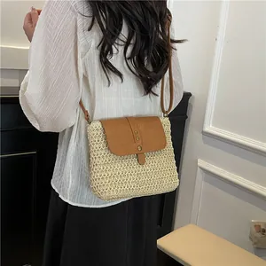 Handwoven straw crossbody bag with brown leather strap worn by a model in a minimalist room