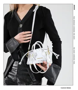 Detail der weißen Mini-Eimertasche mit Schlangenmuster und Mode-Text am Modell