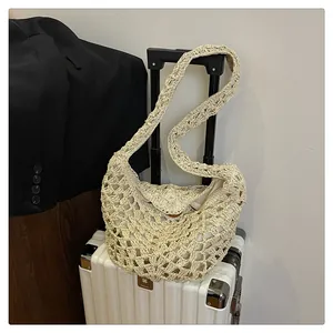 Détail du sac à bandoulière tissé crème avec texture en maille sur une valise blanche