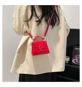 Detail der roten glänzenden Mini-Umhängetasche mit Schnalle auf einem beigen Blazer