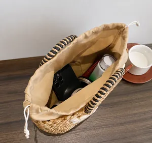 Detailansicht der natürlichen Strohstruktur und des beigen Kordelzugverschlusses der Tasche