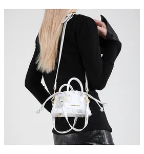 Detail der weißen Handtasche mit Schlangenmuster, Goldaufdruck und schmalem Schultergurt