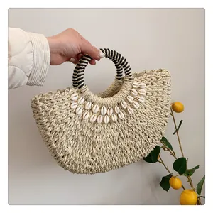 Detail einer Strohhandtasche mit Muschelverzierung und gestreiften Ringgriffen im Fokus