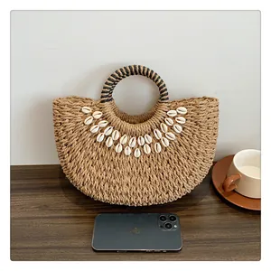 Detail der handgewebten Strohstrandtasche mit natürlichen Muschelakzenten auf Holz