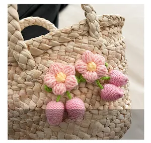 Detail shot of a straw bag featuring pink knitted flowers and a cute fruit charm