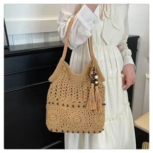 Detailed close-up of hollow crochet texture with fringe tassels on khaki straw shoulder bag