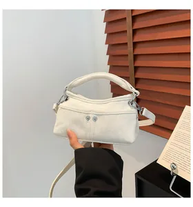 Close-up of a small white canvas crossbody bag with silver rivet details held by hand