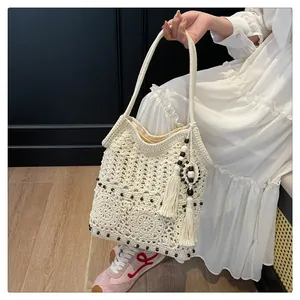 Detail of bohemian knit tote bag showing intricate hollow patterns and beige cotton tassels