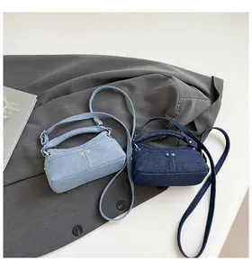 Close-up of denim crossbody bags in light and dark blue with silver studs on white desk