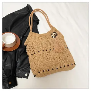 Detail of beige crochet shoulder bag with hollow weaving, dark beads and fringe tassels