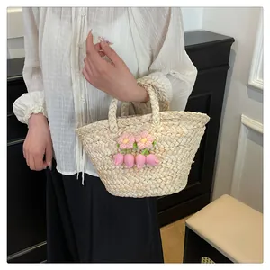 Detail of straw woven handbag featuring crochet pink flower charms and double top handles