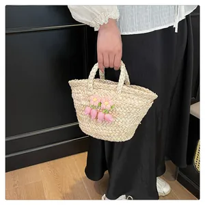 Detail of handmade straw bag with pink crochet flowers and tassels against white shirt