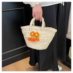Detail of off-white straw tote bag with knitted orange flowers and carrot charms