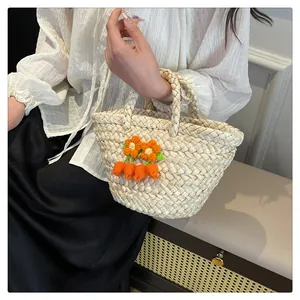 Detail of hand-woven straw tote bag with crochet flowers and carrot charms
