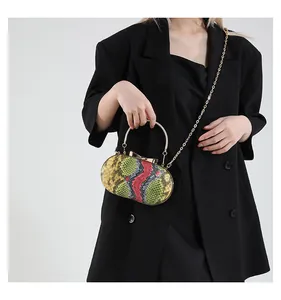 Detail of a snake-skin pattern oval clutch with gold handle worn with a black suit