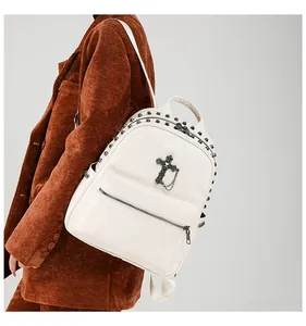 Close-up of a white leather backpack featuring dark metal studs and a black cross chain charm