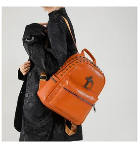 Detail showing orange pebble leather backpack with black rivets and cross chain accessory