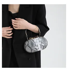 Detailed close-up of snake print clutch bag featuring golden bow clasp and circular handle