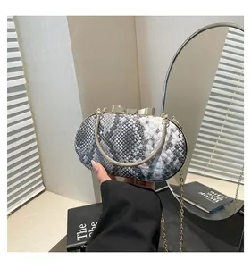 Detail of snake print clutch bag with gold bow clasp and metallic handle texture
