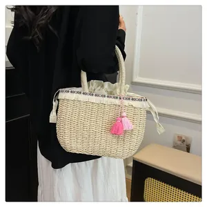 Dettaglio borsa in paglia con bordo etnico, nappe beige e ciondoli rosa