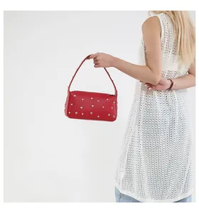 Red lychee grain leather baguette bag with silver rivets carried by model in white vest