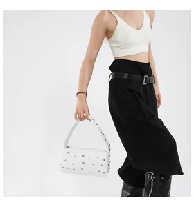 Detail of white leather baguette bag with silver rivets shown on a stylish model