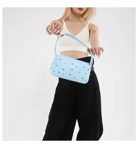 Detail of light blue baguette bag with silver rivets carried by a model on white background